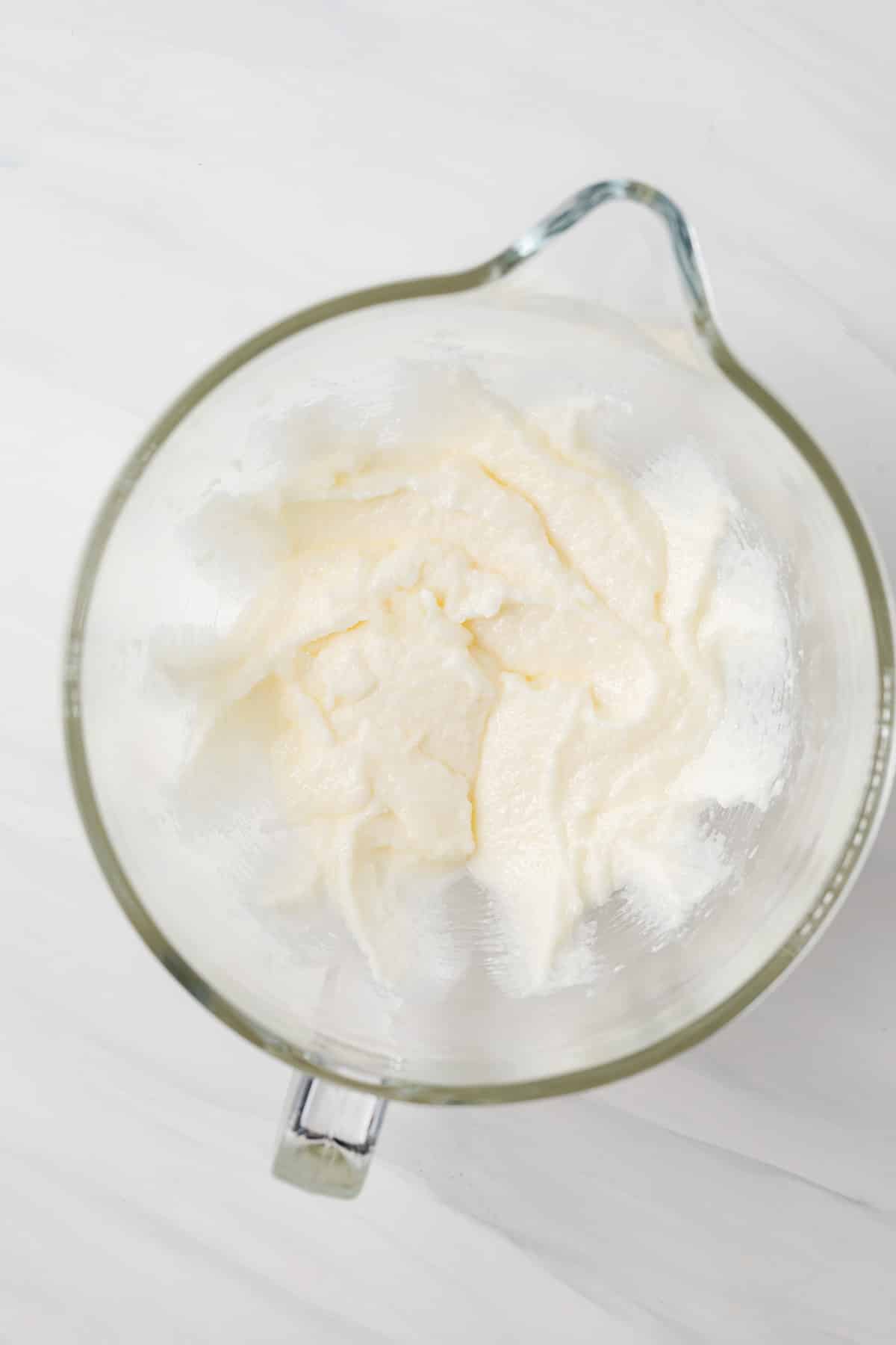 Butter, oil, and sugar creamed in glass bowl.
