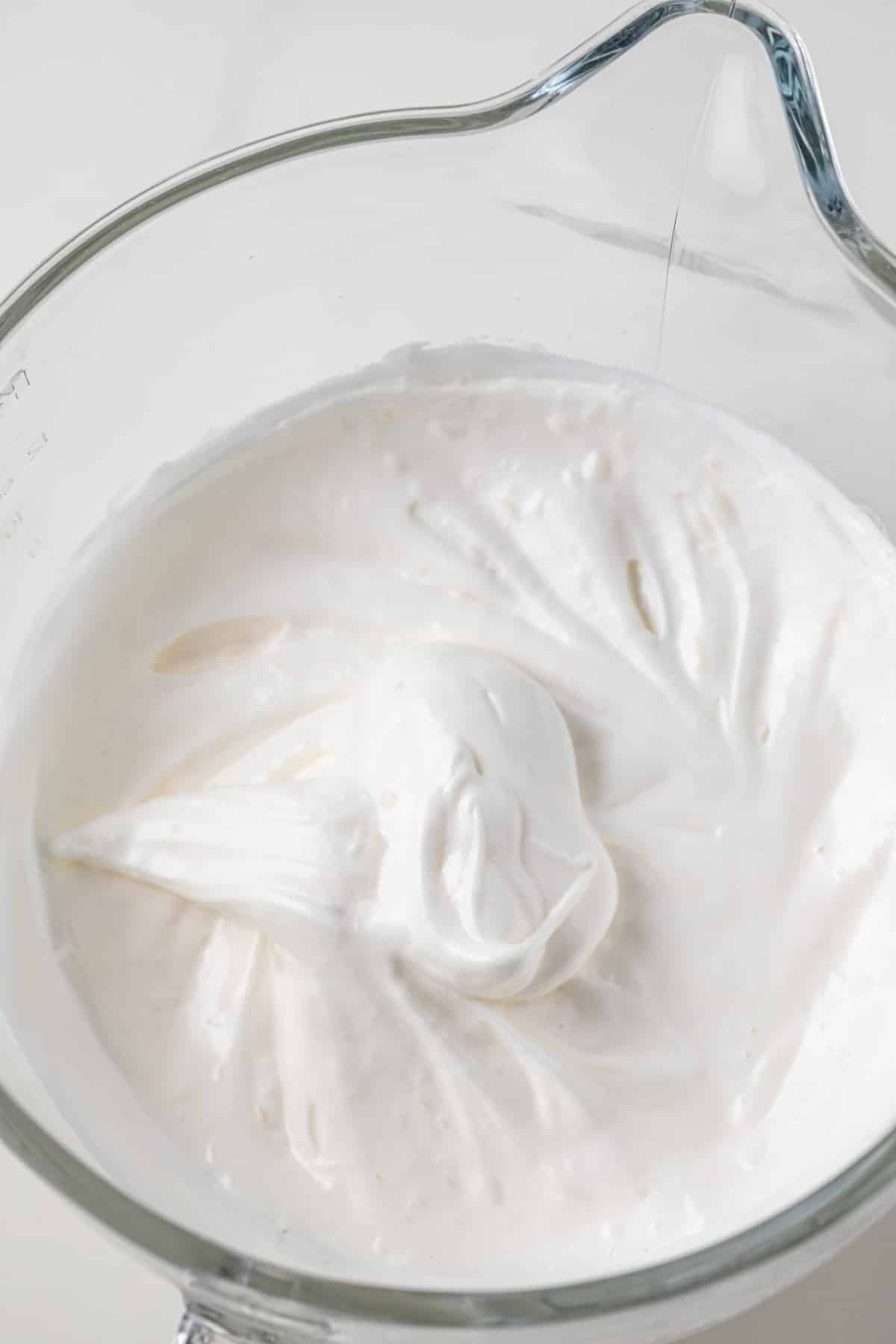 Egg whites whipped to stiff peaks in a glass bowl.
