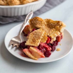 side view of a slice of apple cranberry pie on a white plate