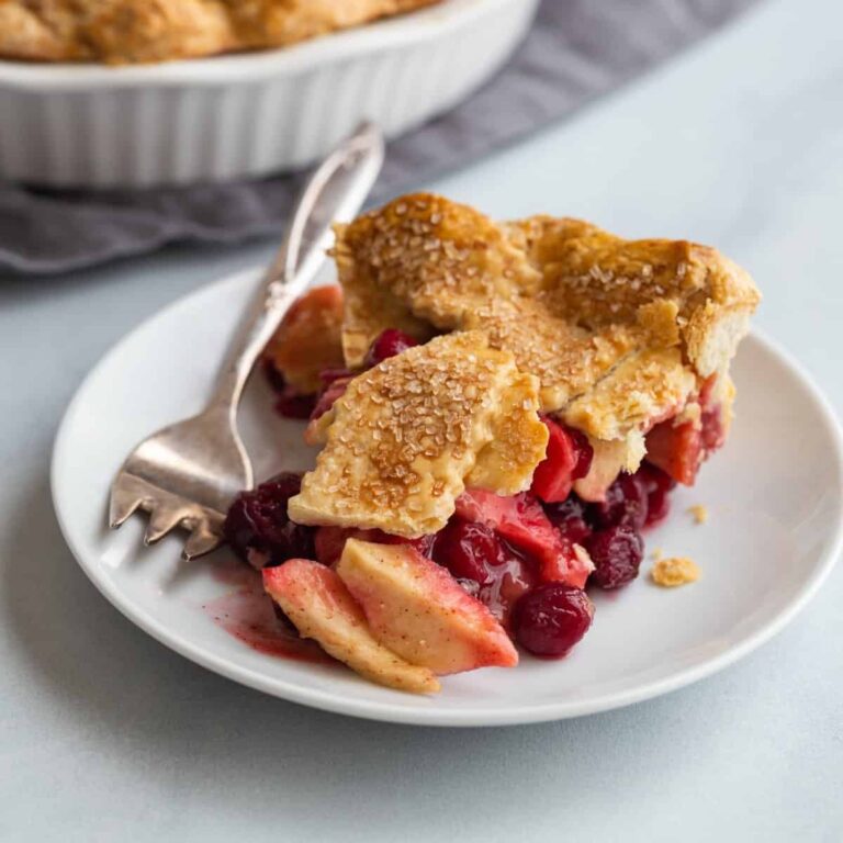 side view of a slice of apple cranberry pie on a white plate