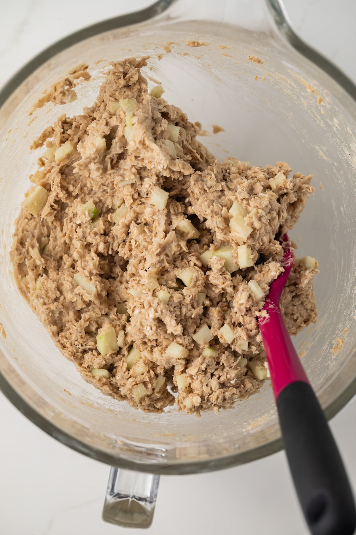 Apple oatmeal cookie dough in glass bowl with spatula.