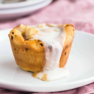 Close up view of Apple Pie Cinnamon Roll Cup on a white plate with glaze dripping down the side.