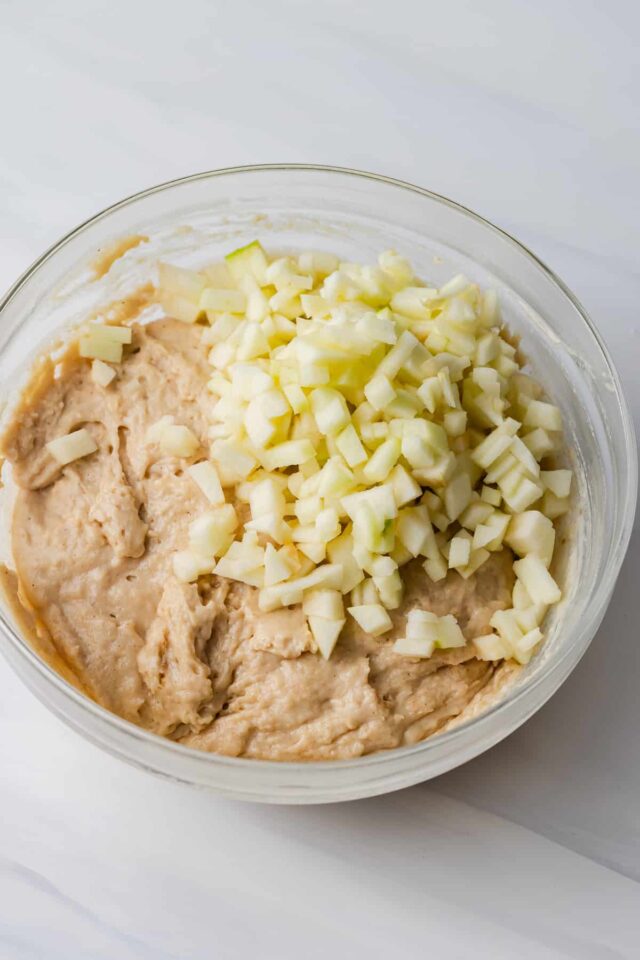 Apple chopped on top of muffin batter in a bowl
