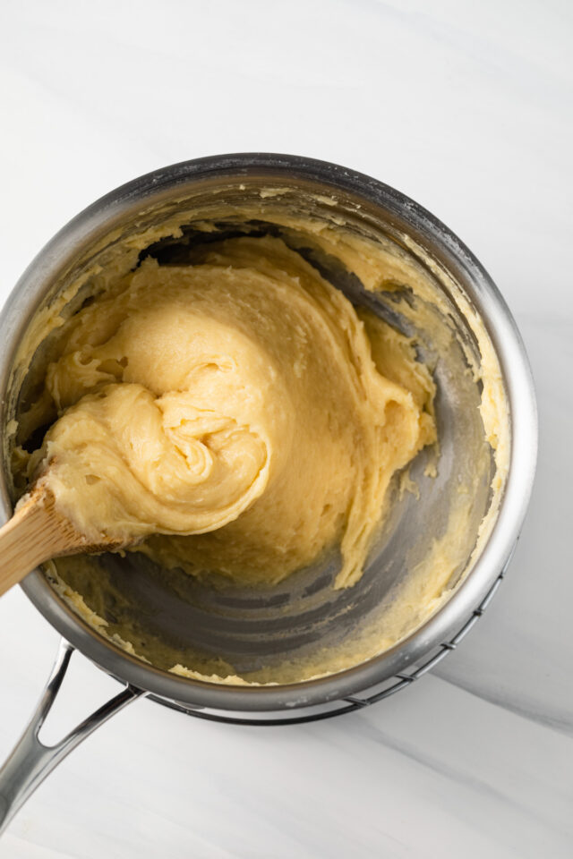 A wooden spoon stirring pate choux dough.