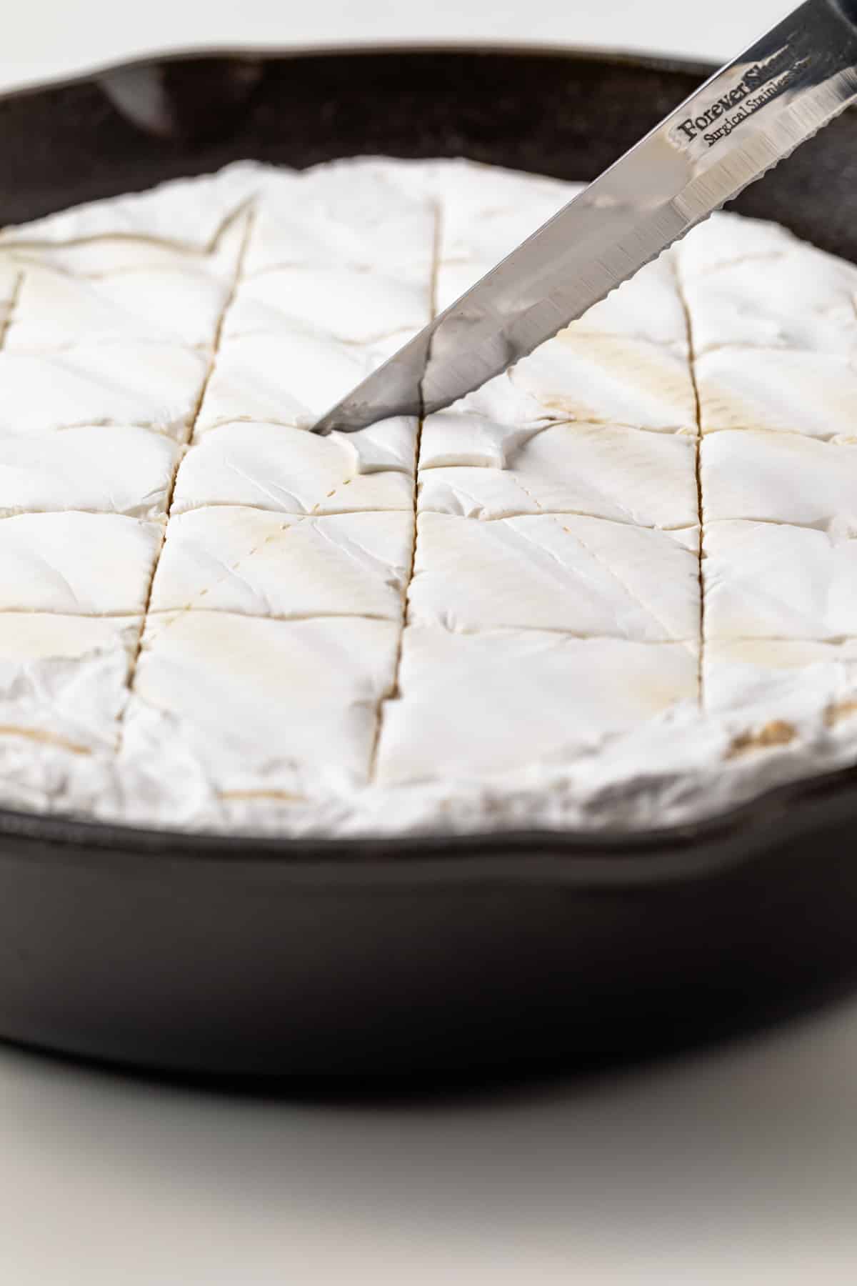 Knife scoring wheel of brie in cast iron skillet.