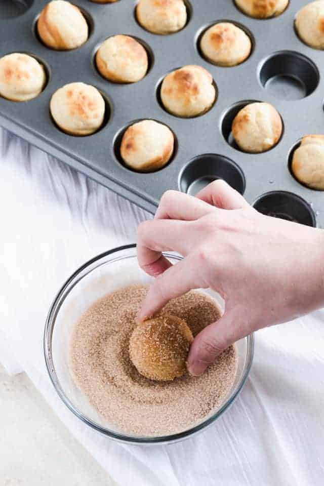 Baked Bunuelos being rolled in cinnamon sugar.