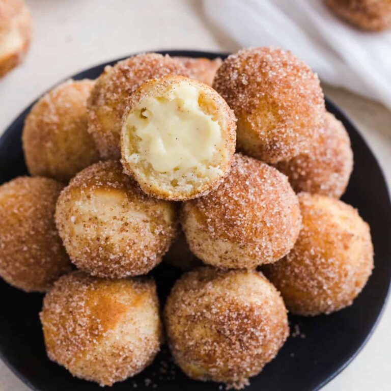 Close up of baked bunuelos with anise filling on a black plate.