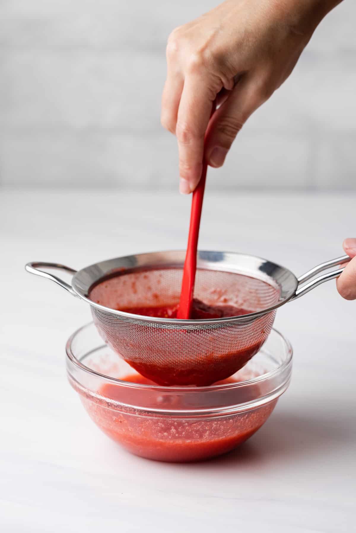 Strawberry puree being pushed through a mesh sieve