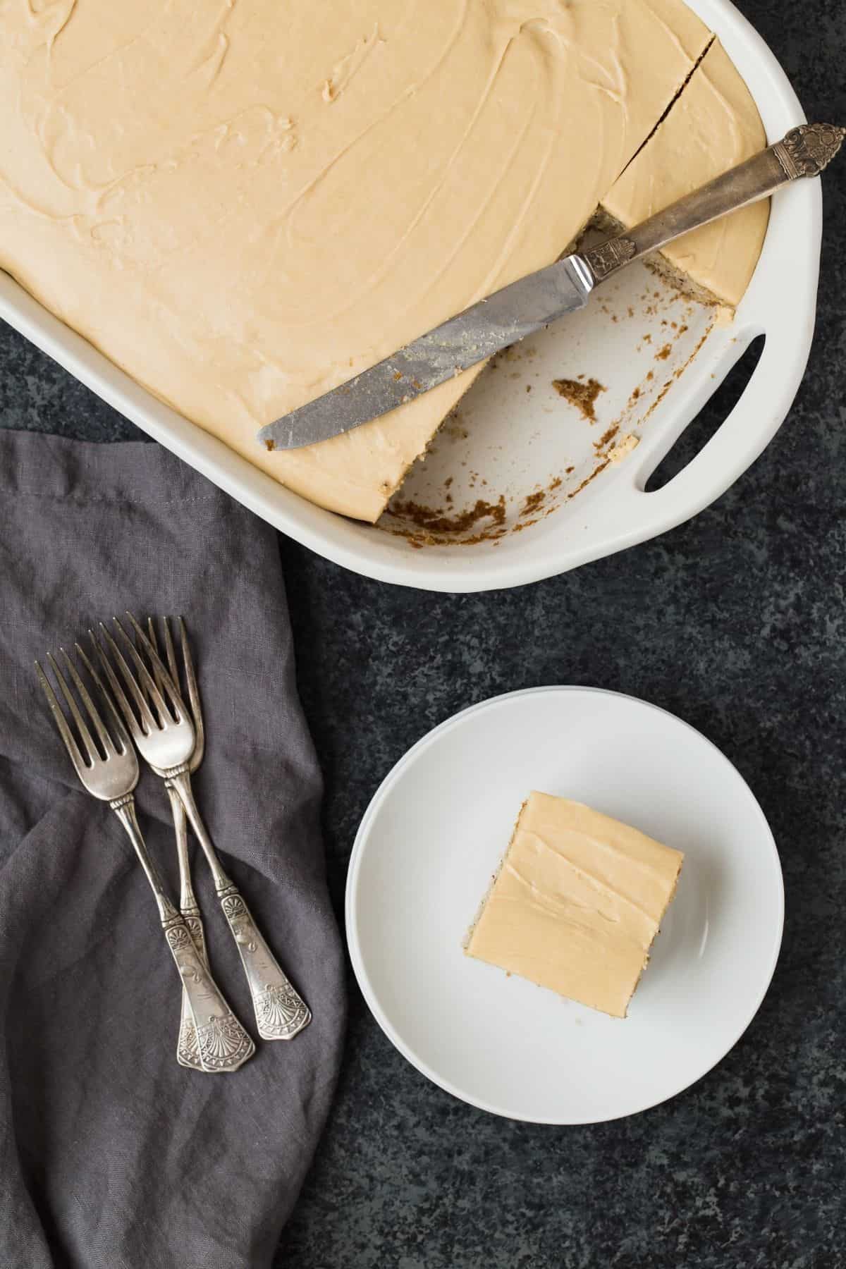 Easy Banana Cake in a white cake pan next to a slice of banana cake on a plate.