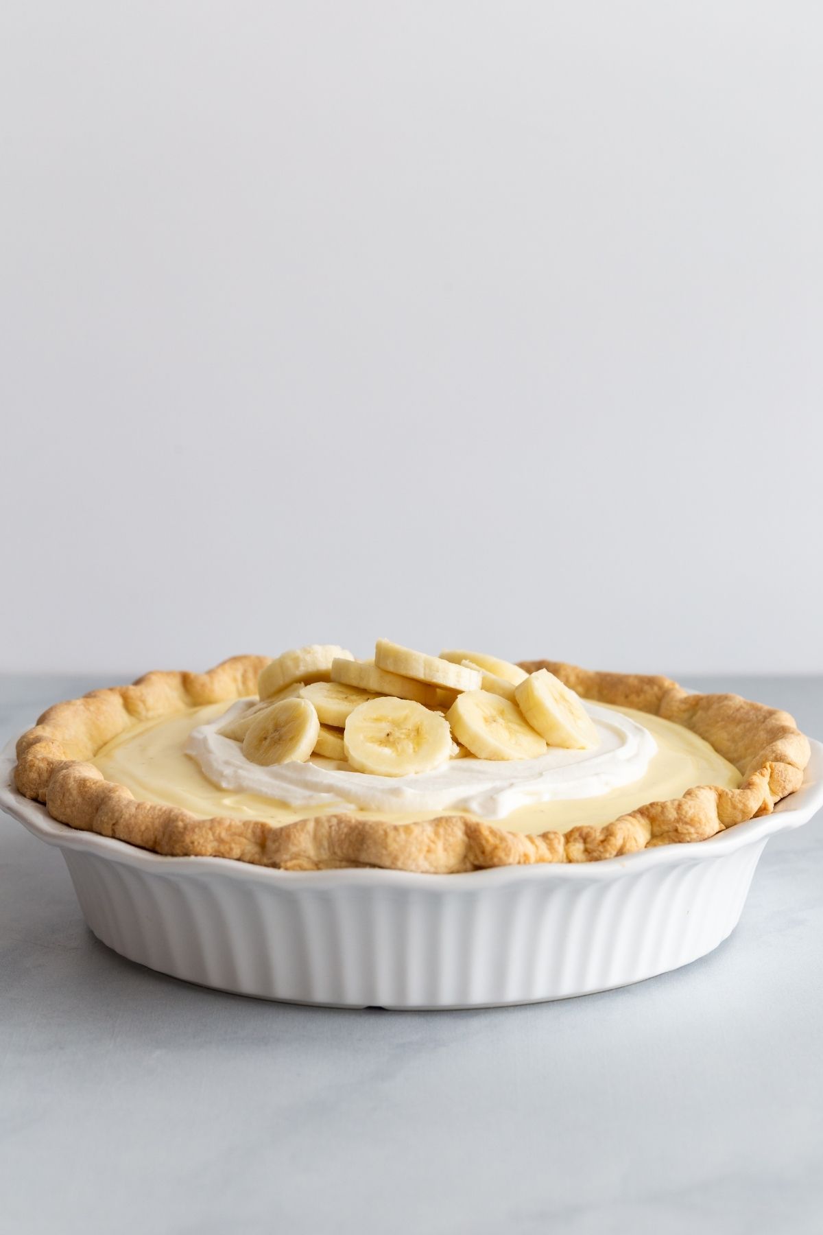 Side view of banana cream pie in a white pie dish.