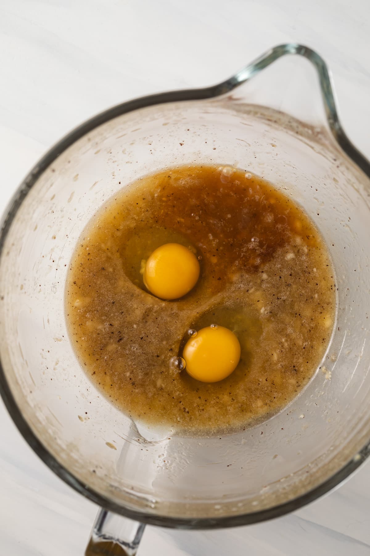 Mashed banana with brown butter, eggs, and vanilla in mixing bowl.