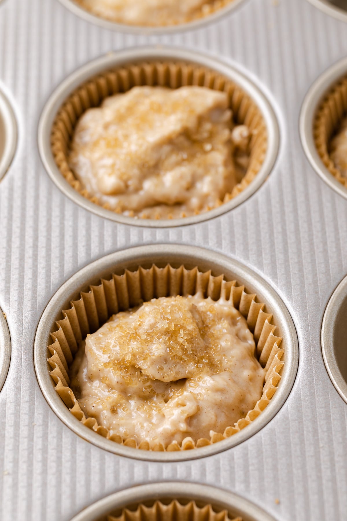 muffin batter topped with coarse sugar in muffin pan lined with paper liners