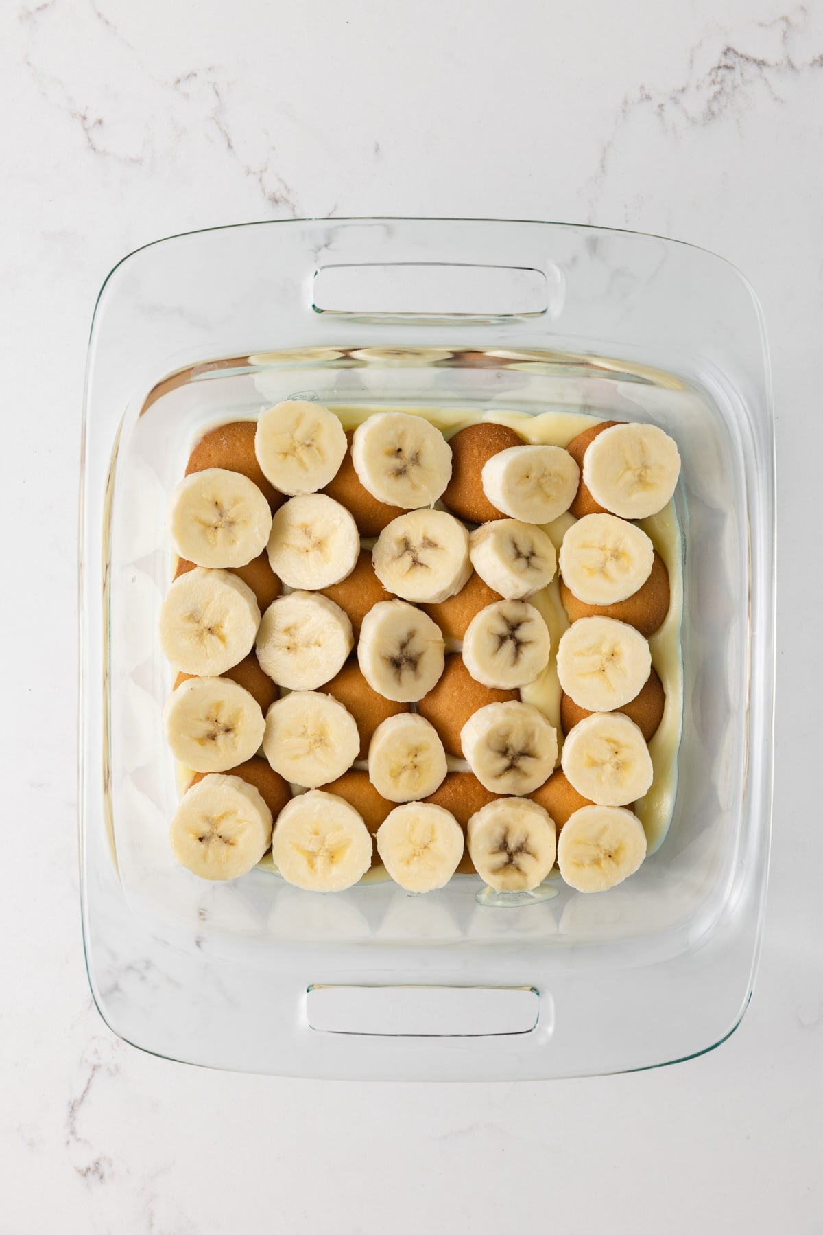 Vanilla pudding, vanilla wafers, and bananas in a glass dish.