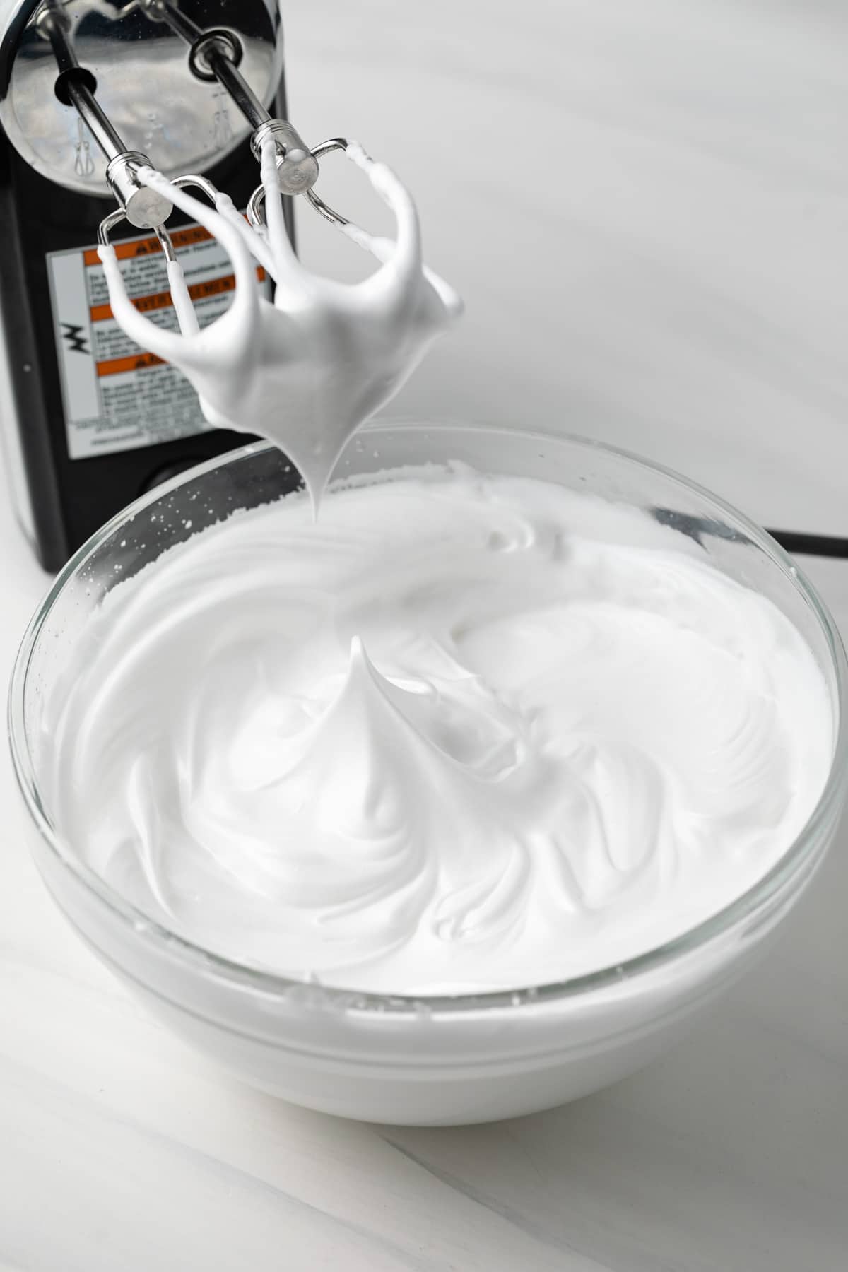 Meringue frosting in glass bowl with mixer.