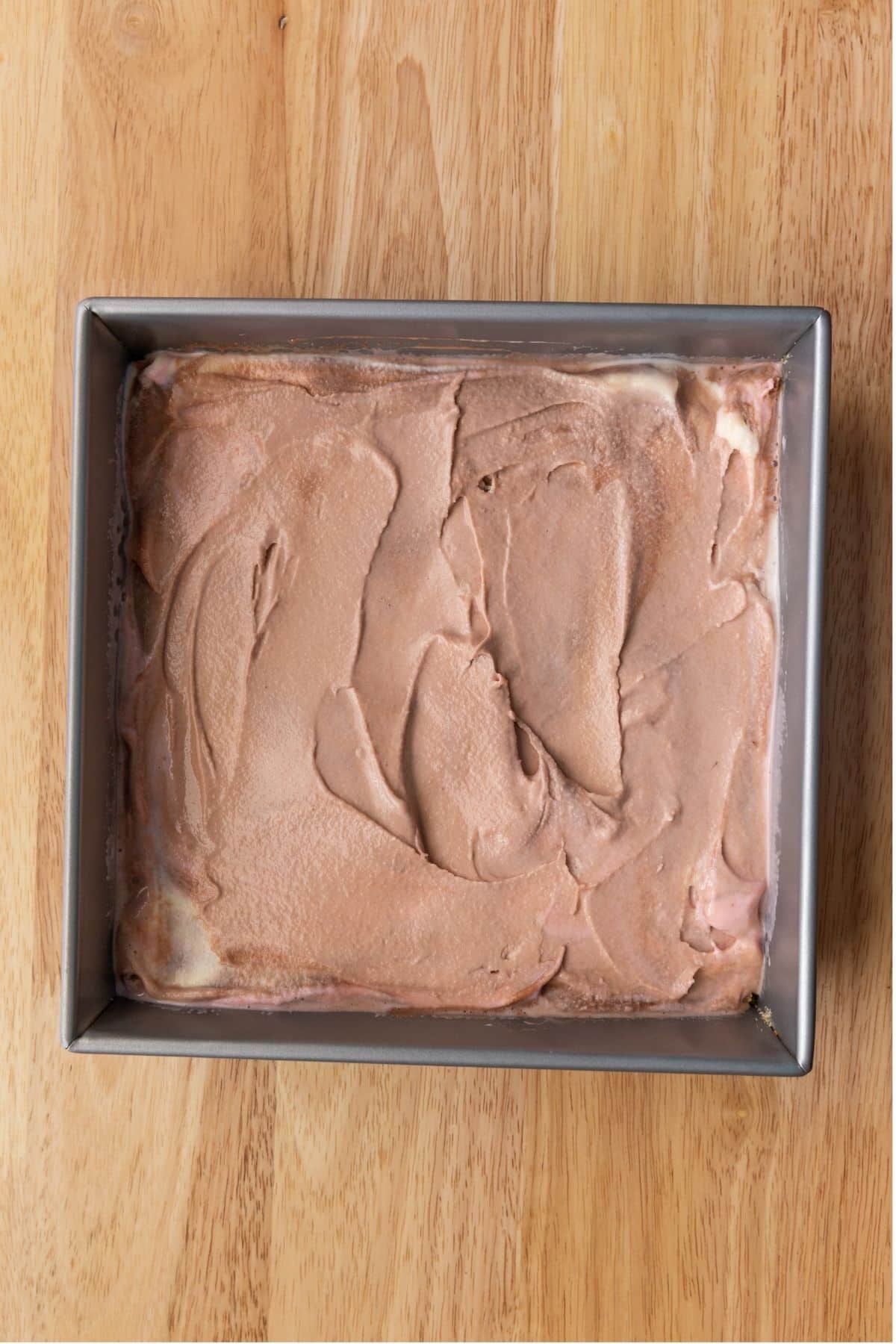 Ice cream over graham cracker crumbs in square pan.