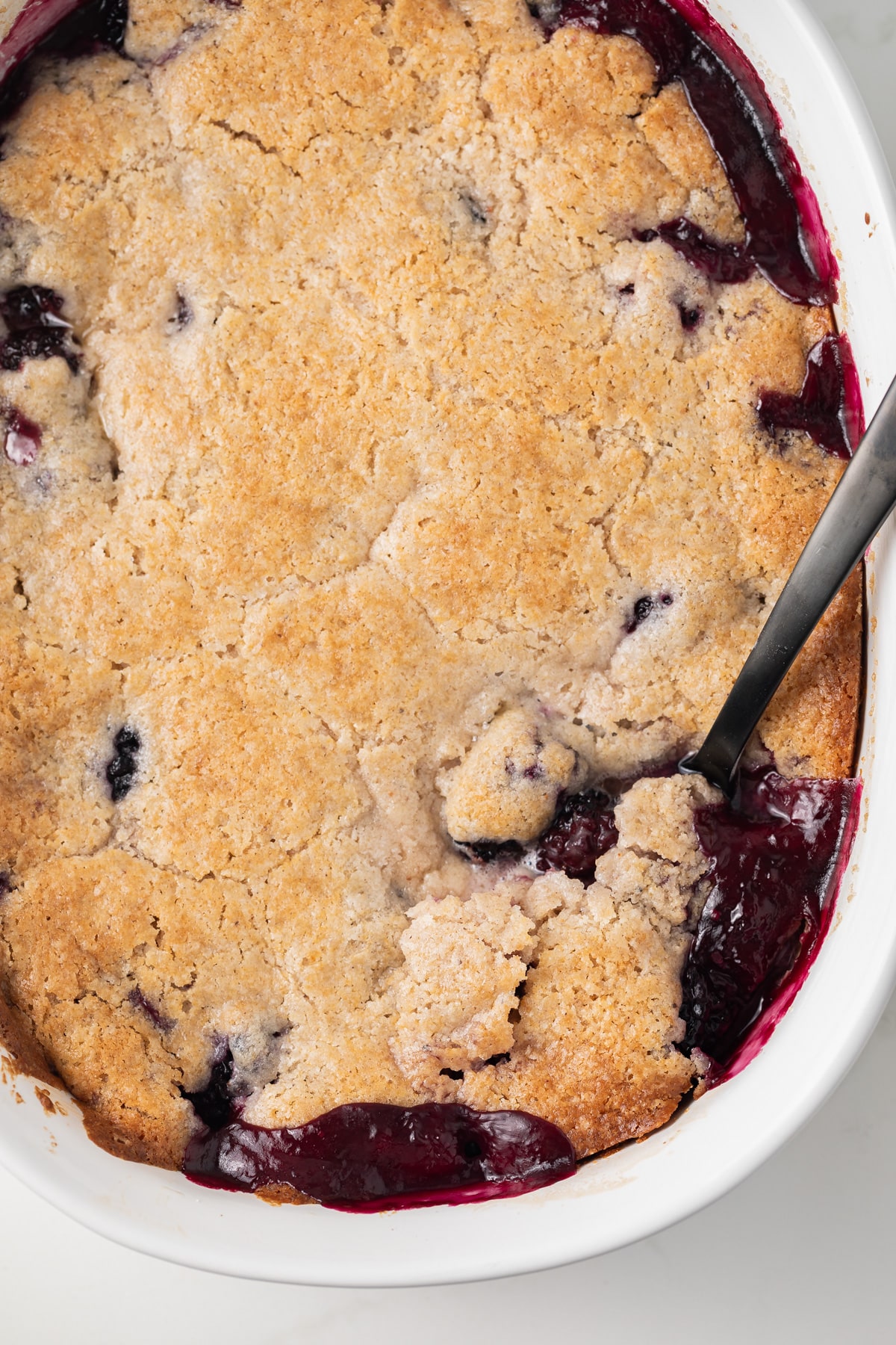 Spoon taking out a scoop of blackberry cobber.