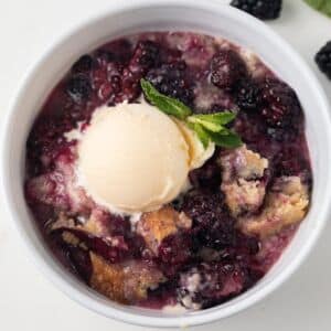 Blackberry cobbler in white bowl with scoop of vanilla ice cream.