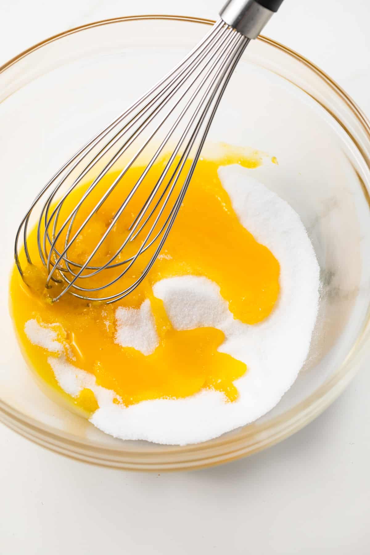Egg yolks and sugar in glass bowl with whisk.