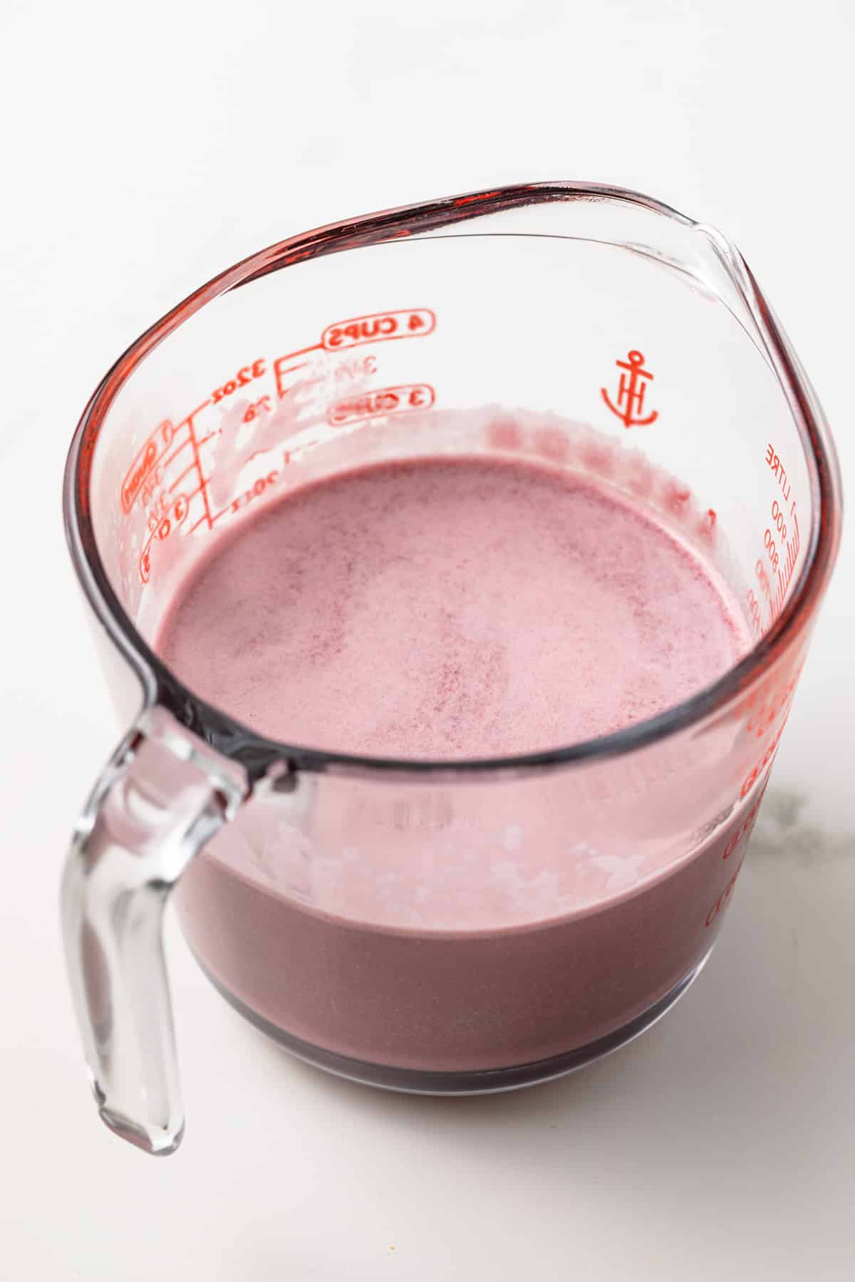 Glass measuring cup filled with blackberry custard.
