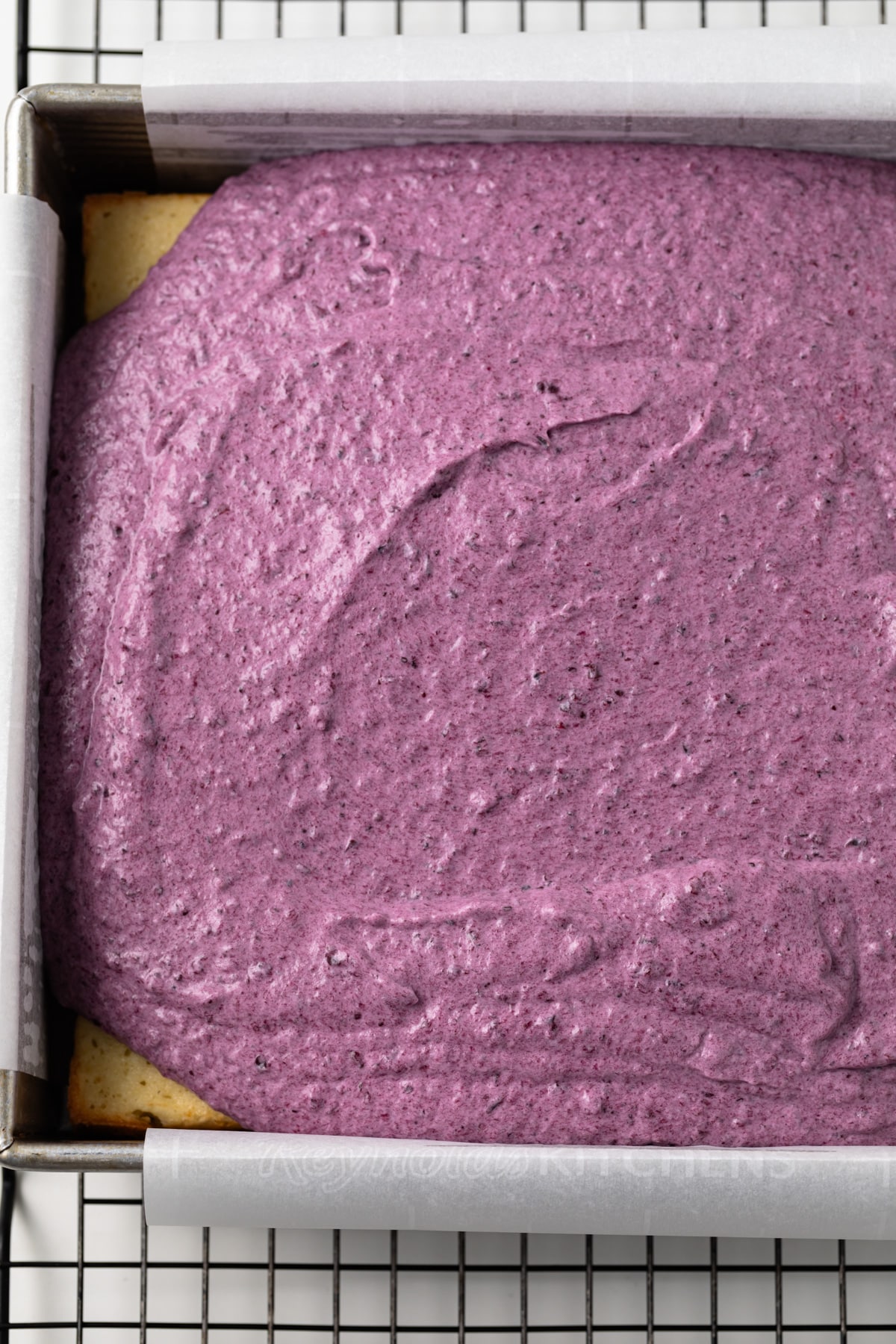 Yellow cake topped with blueberry mousse in cake pan.