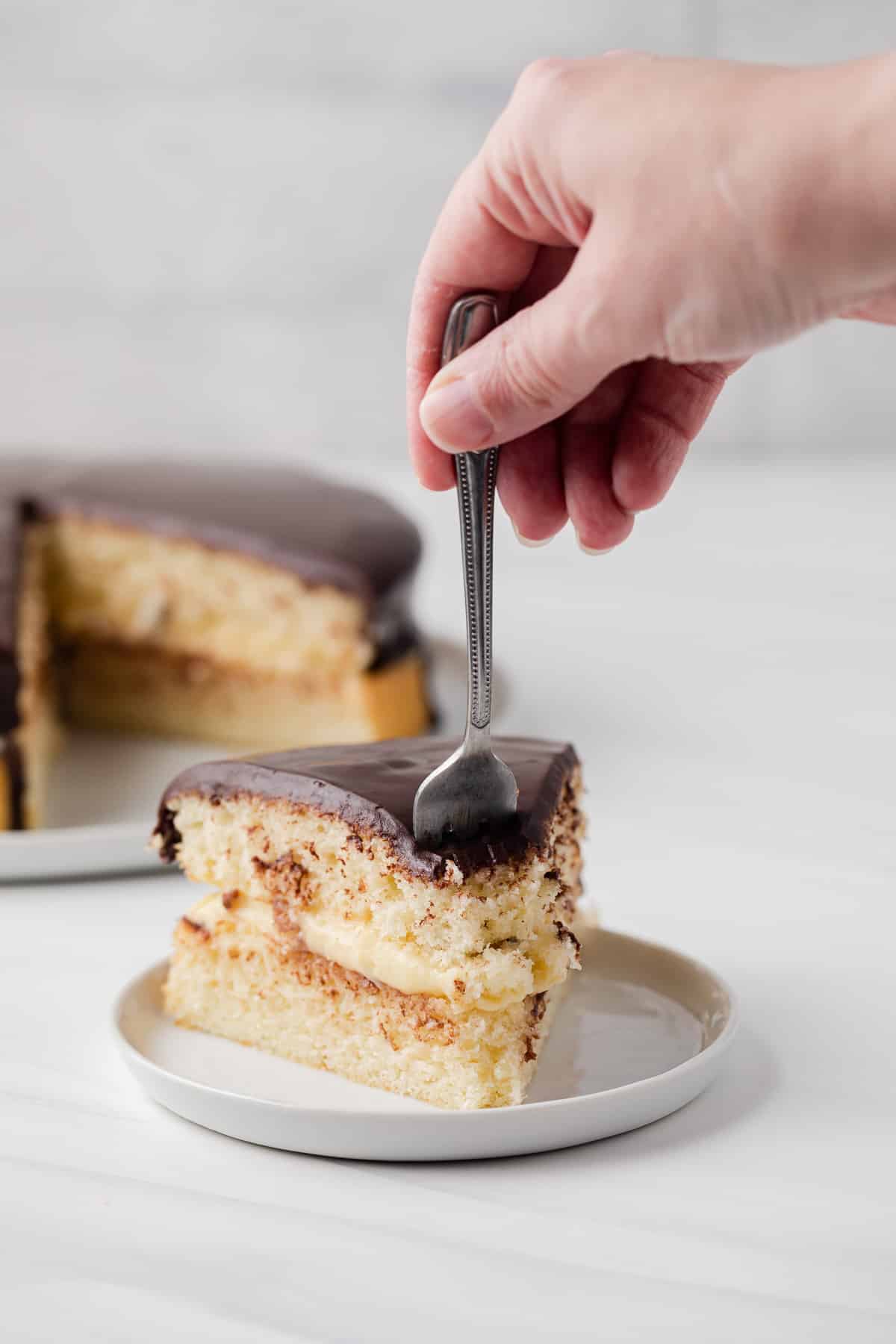 Fork taking a bite out of boston cream pie slice.