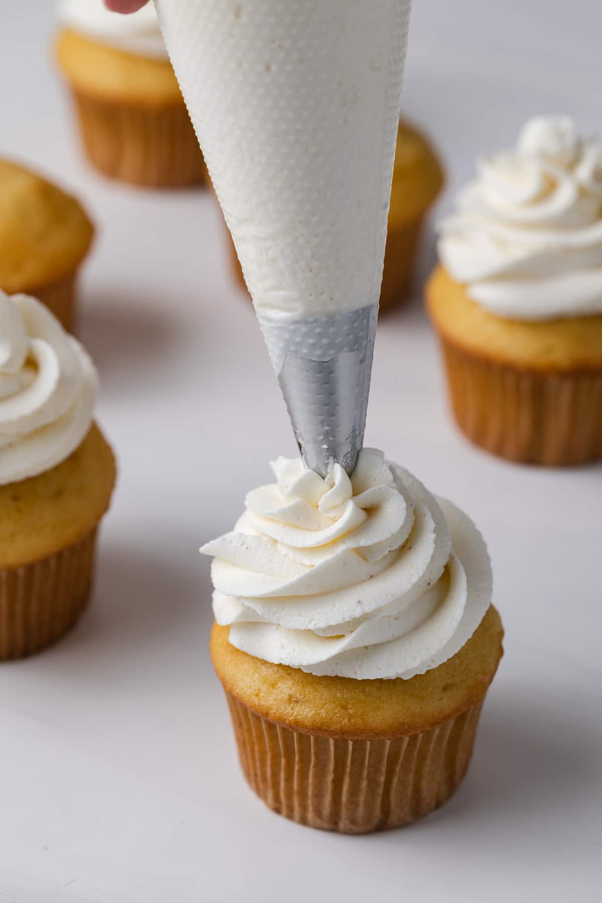 brown butter buttercream being piped in a swirl on top of vanilla cupcake