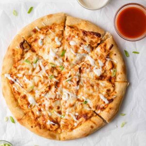 overhead view of buffalo chicken pizza cut into slices on white parchment paper