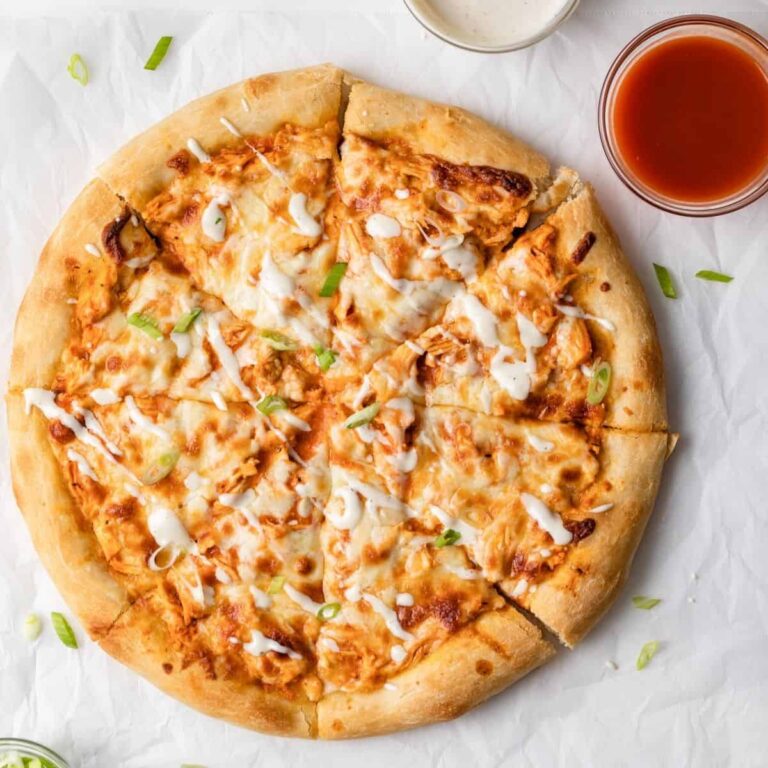 overhead view of buffalo chicken pizza cut into slices on white parchment paper