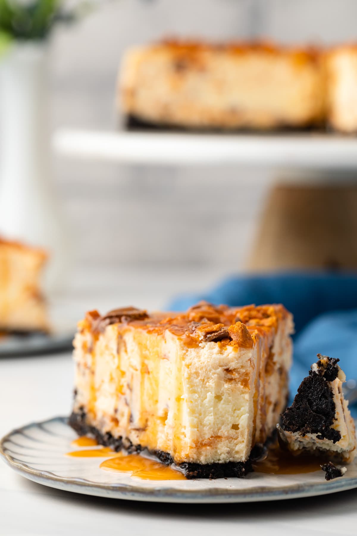 Fork taking a bite out of slice of butterfinger cheesecake.