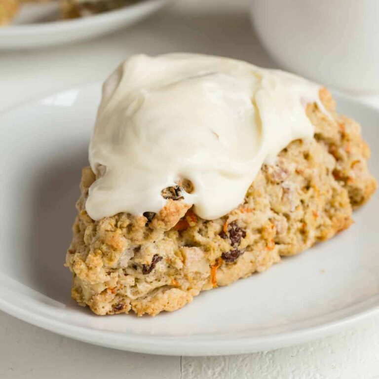 A carrot cake scone topped with cream cheese icing on a white plate.