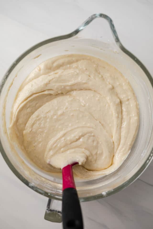 Vanilla cake batter in a glass bowl with pink spatula.