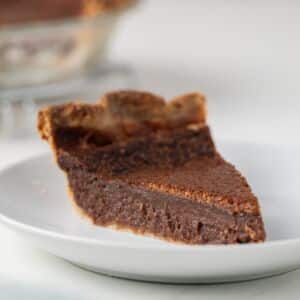 Side view of a slice of chocolate chess pie on white plate.