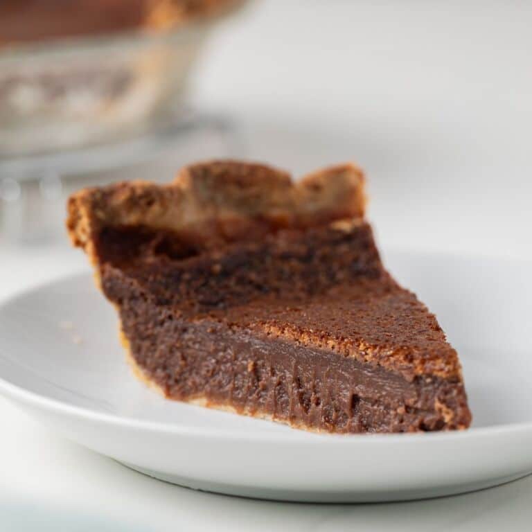 Side view of a slice of chocolate chess pie on white plate.
