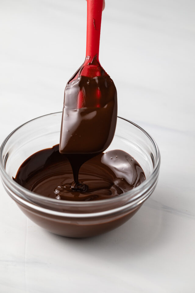 A bowl of melted chocolate with some falling off a spatula