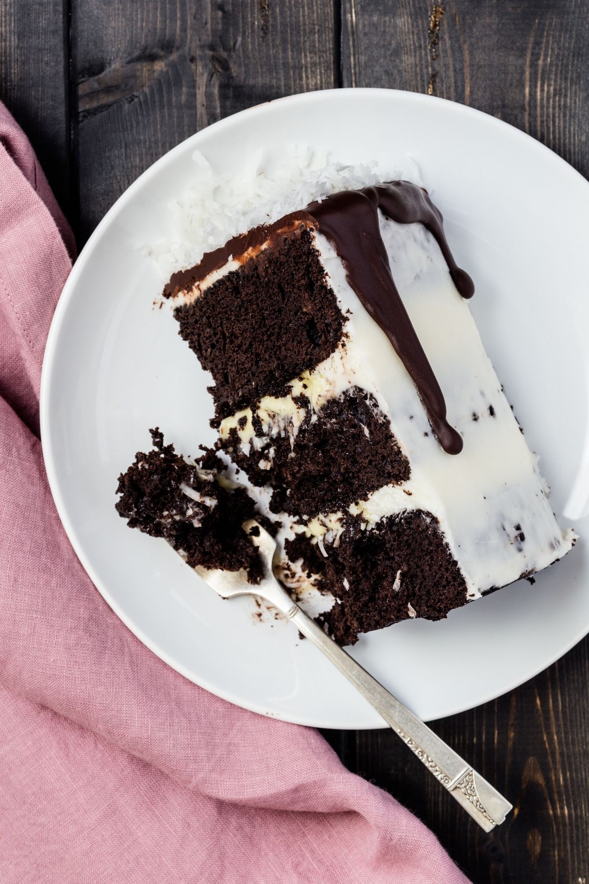 A slice of three layer coconut cake on a white plate with a fork taking out a bite.