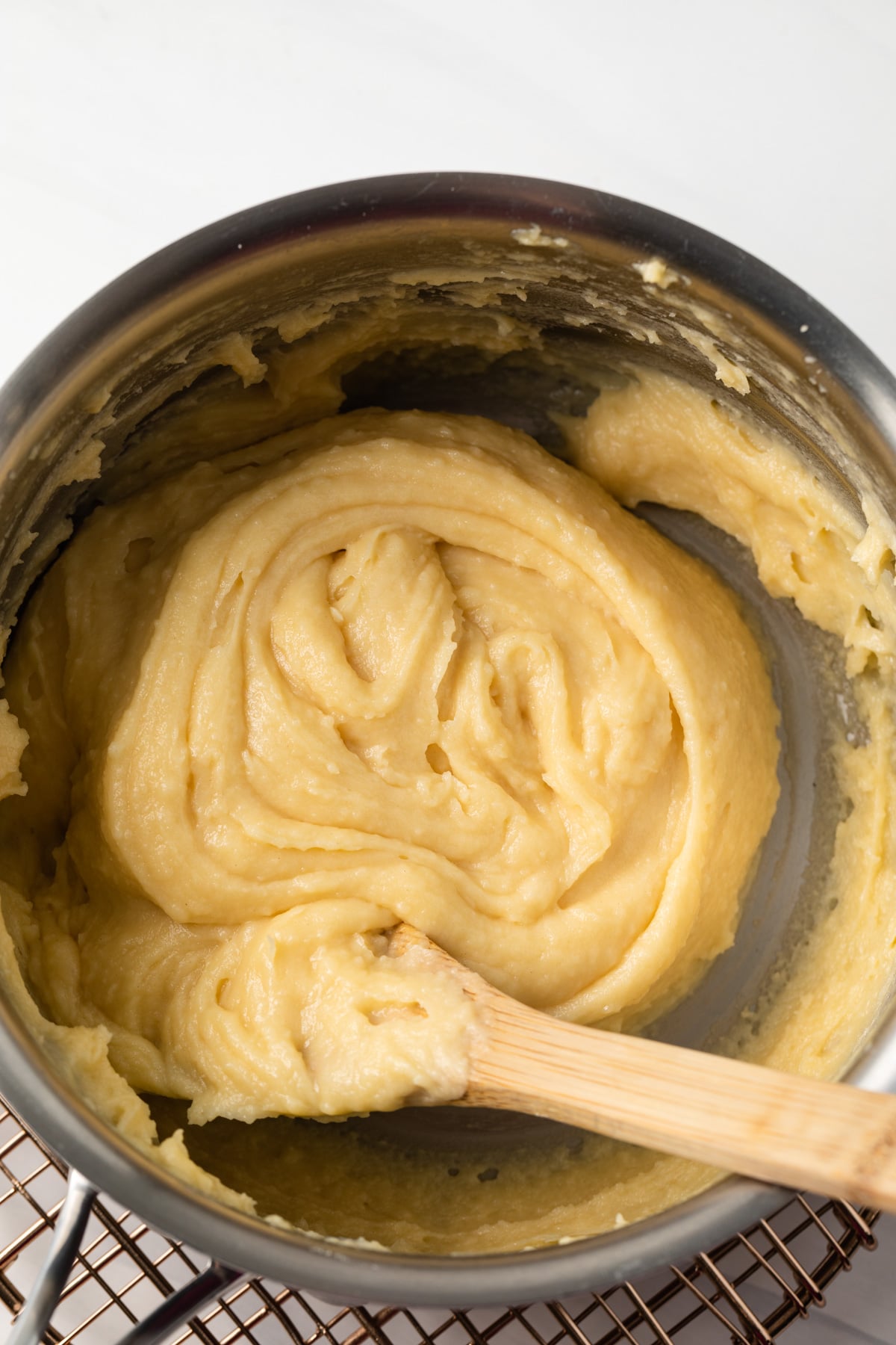 Pate a choux in pot with wooden spoon.