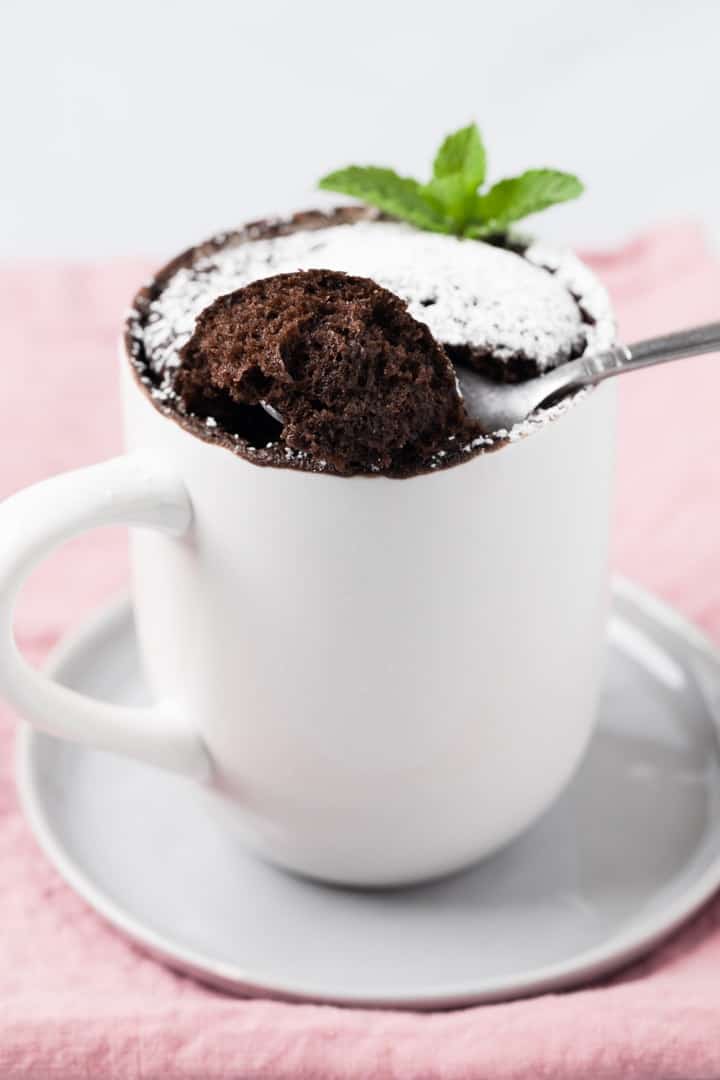 a spoon taking a bite out of chocolate mug cake dusted powdered sugar