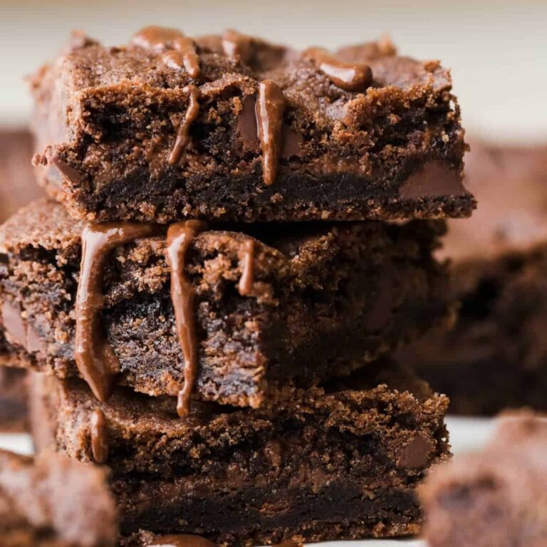 Three chocolate nutella cookie bars stacked on white parchment paper and drizzled with nutella.