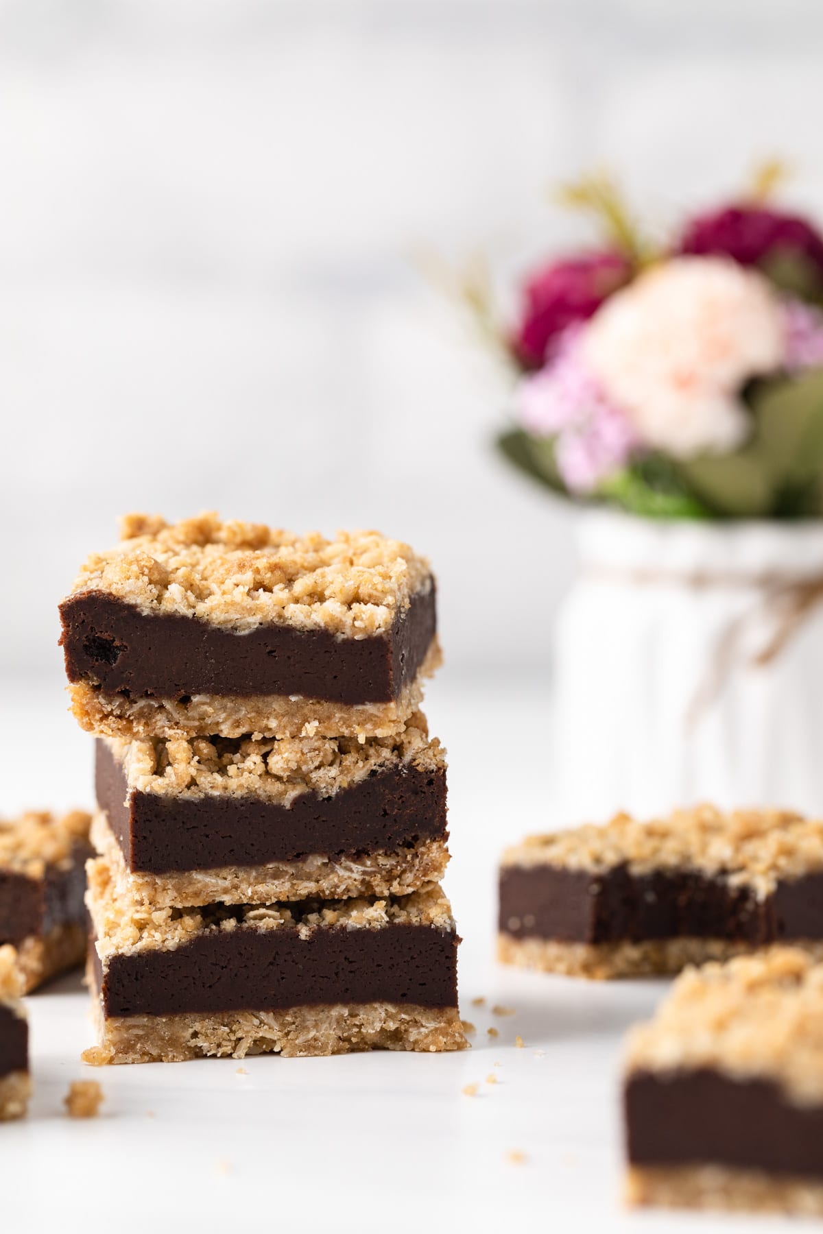 three chocolate oatmeal bars stacked next to flowers in vase and more oat bars