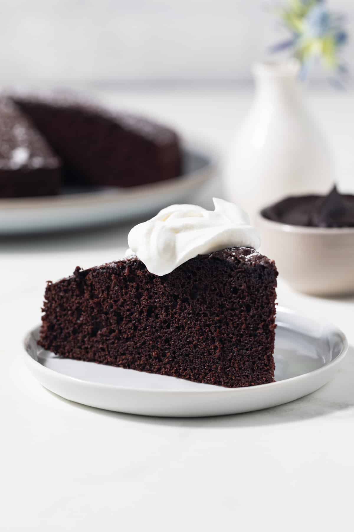 Slice of chocolate olive oil cake with whipped cream on top.