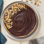 Overhead view of chocolate peanut butter cheesecake on a white plate with a blue napkin beside it.