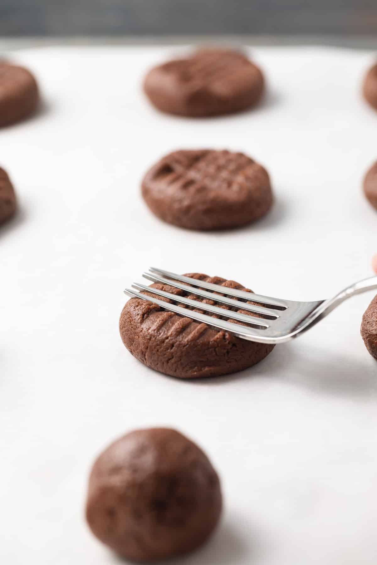 Pressing chocolate peanut butter cookie dough balls with tines of a fork.