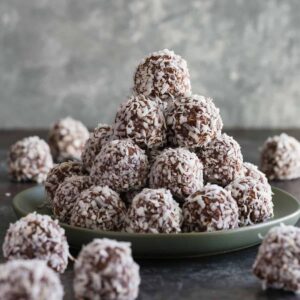 Chocolate peanut butter balls rolled in coconut stacked neatly on a green plate.