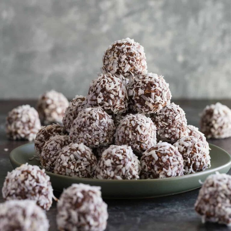 Chocolate peanut butter balls rolled in coconut stacked neatly on a green plate.