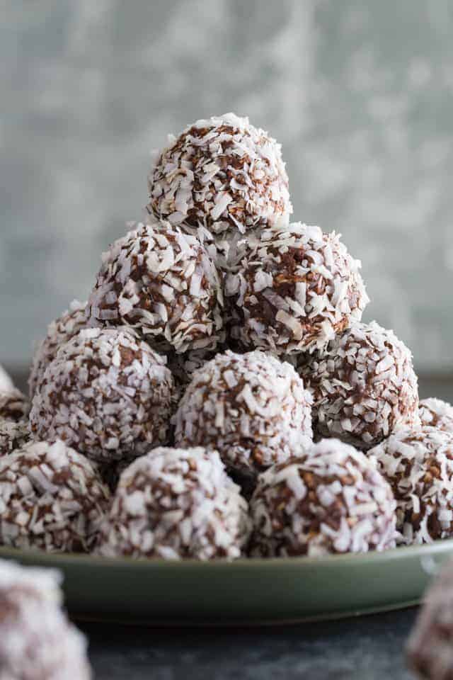 Close up view of chocolate peanut butter balls rolled in coconut stacked neatly on a green plate.