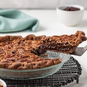 Slice of chocolate pecan pie lifted out of whole pie.