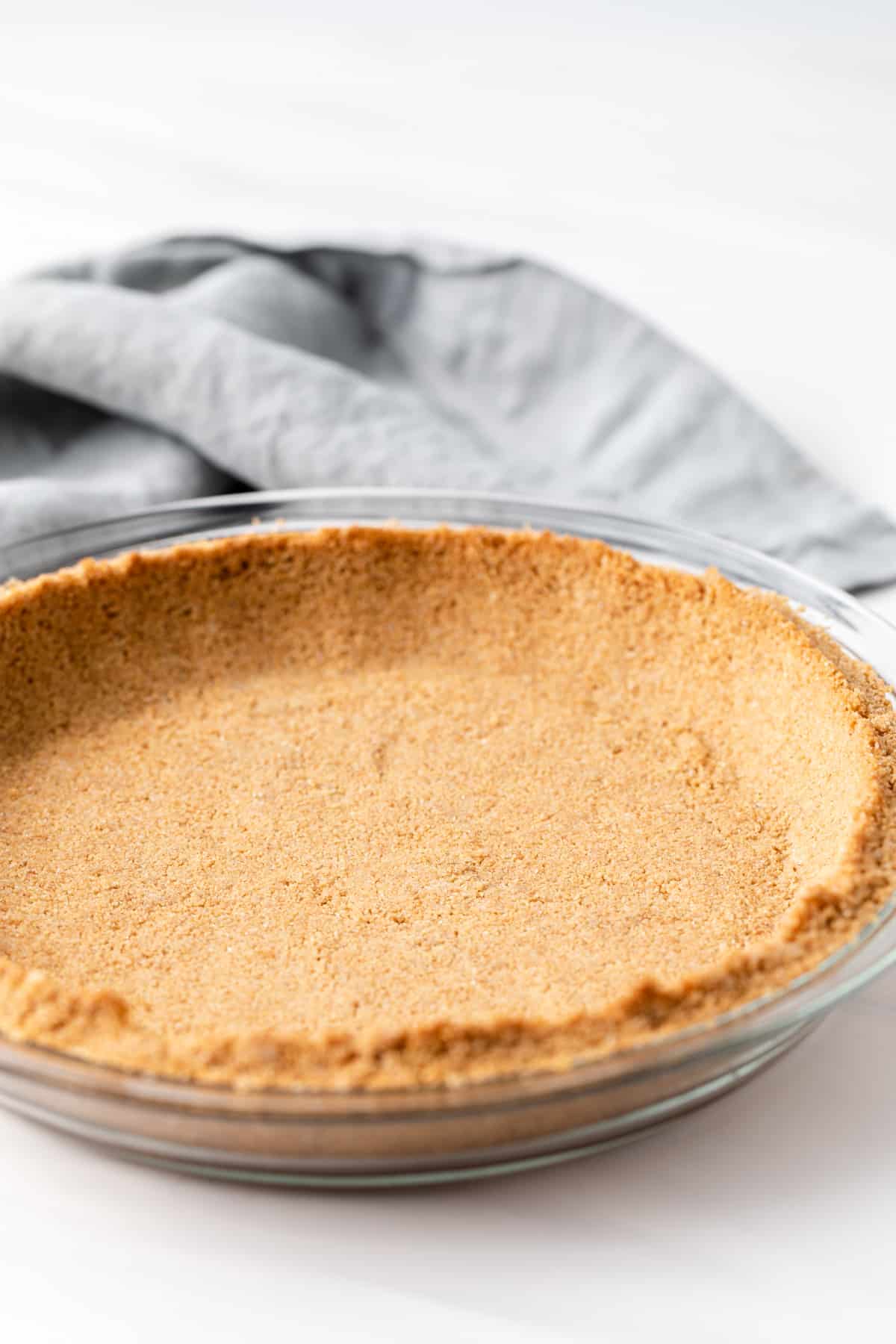 graham cracker crust in glass pie plate with grey napkin