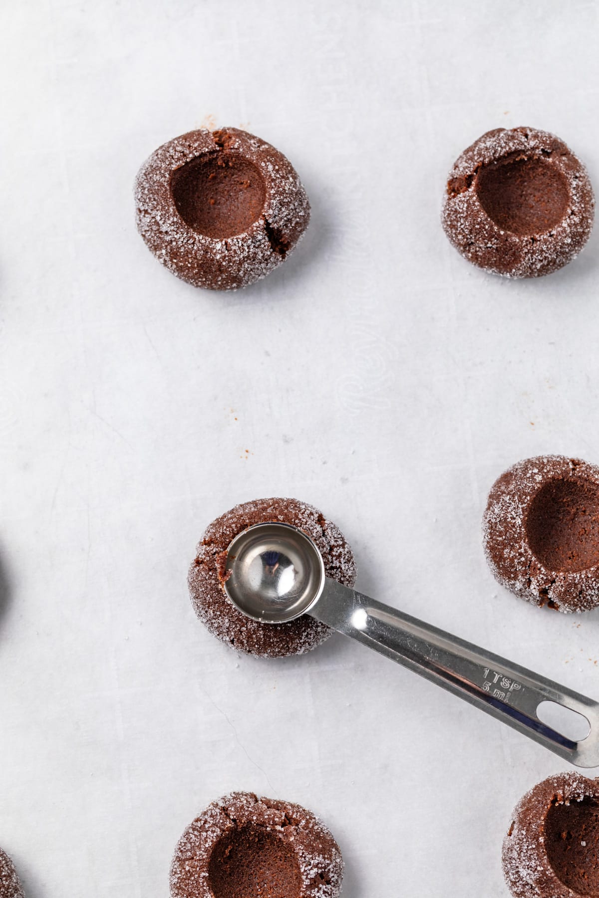 Teaspoon pressing a cavity into cookie dough balls.