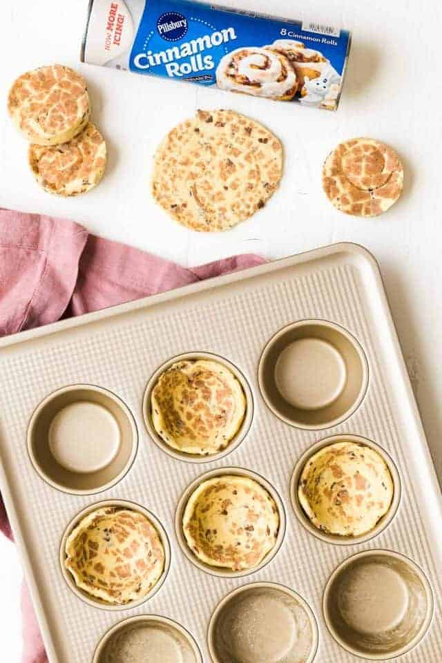 Cinnamon roll dough being pressed into a muffin gold muffin tin.