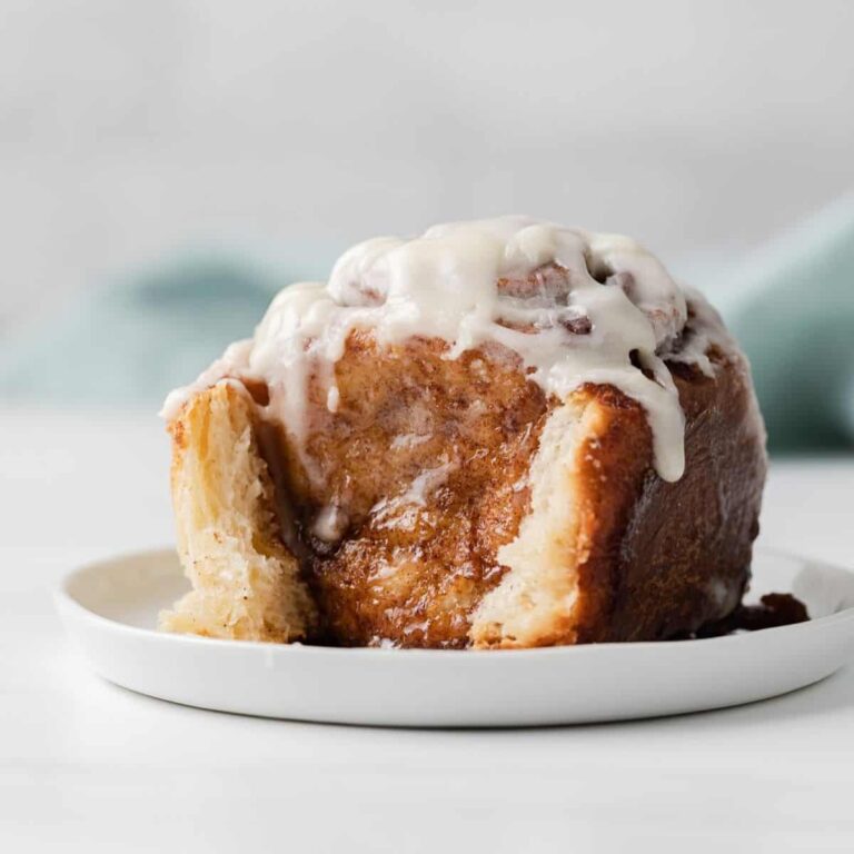 side view of a single cinnamon roll on a white plate with teal napkin behind